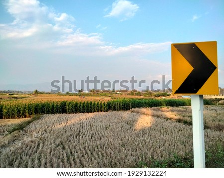 Arrow traffic sign beside the rural road in Thailand.  Agriculture farm land  and sky background. 