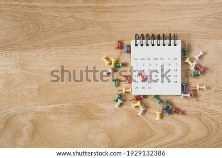 red thumbtack on white page calendar and multicolor on grunge wood background , top view