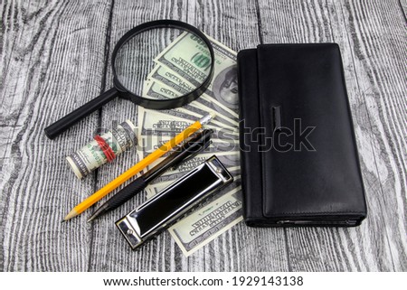 Financial, business success or analysis concept with 100 dollar bills fanned below a purse with magnifying glass, pen and pencil on a decorative wood background in a high angle view
