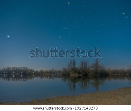 The Orion constellation in a full moon night over the quarry lake Binsfeldsee near Speyer in Germany.
