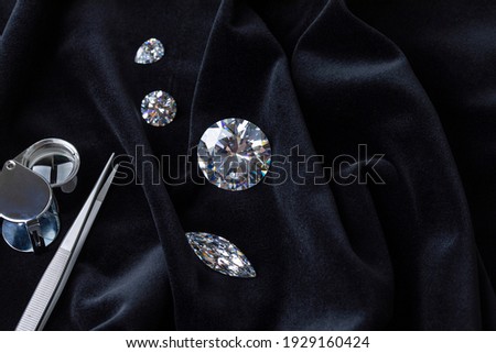 Close up of polished diamonds different cuts and sizes with tweezers and magnifying glass on black velvet fabric top view with copy space. Royalty-Free Stock Photo #1929160424