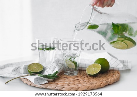 Detox water with lime fruit. Hand pouring lime fruit water from jug into glasses. Royalty-Free Stock Photo #1929173564