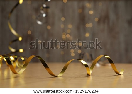 Shiny golden serpentine streamer on wooden table against blurred lights. Space for text Royalty-Free Stock Photo #1929176234