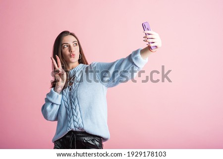 Portrait of a brunette girl on a pink background who takes a selfie on a smartphone