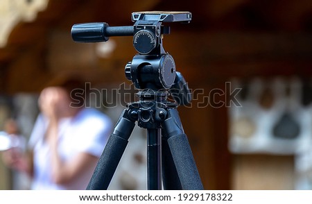 Large black professional tripod with swivel head on a busy street