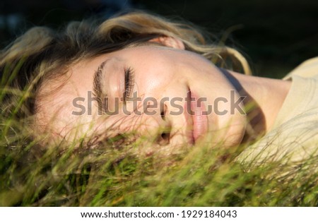 close-up of a beautiful teenage girl lying on green grass over sunlight. Eyes closed, enjoying nature outdoors. Cute teenage girl relaxing daydreaming in the park. Spring, summer, sunbathing Royalty-Free Stock Photo #1929184043