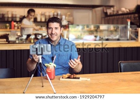 Social media influencer or food blogger creating content inside small restaurant – man sharing live food review using smartphone on tripod and microphone – Owner promoting small business online