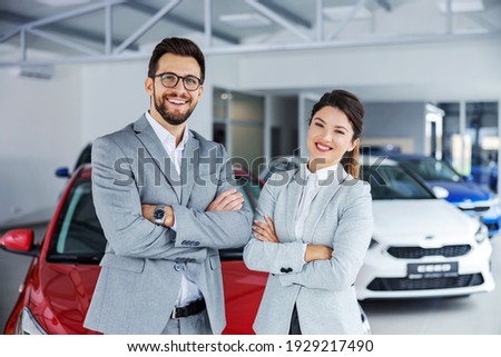Smiling, friendly car sellers standing in car salon with arms crossed and announcing retail. Royalty-Free Stock Photo #1929217490