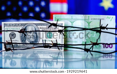 US Dollar and EU currency wrapped in barbed wire against United States and European Union flags as symbol of joint economic warfare, sanctions and embargo busting. Close up.