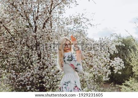 Gentle portrait of a blonde in a white dress near a blooming rose tree in spring
