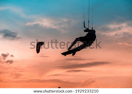Kitesurfing jump, man kite surfing at sunset, golden hour jumping silhouette on an orange background. Kite surfer performing jump tricks board off and board grab. Kiteboarding landscape picture.