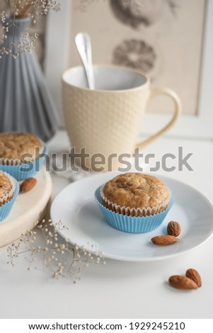 Homemade fresh baked cupcakes muffins in blue liners arranged on a table with cup of tea coffee almonds vase with dry flowers and picture frames in the blurred background