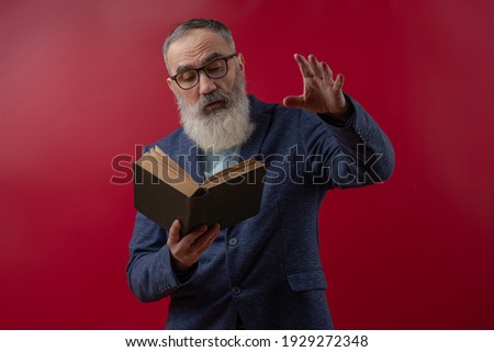 Senior charismatic man with a gray beard in a light shirt in a dark casual jacket holding a book and gestures, reciting poems, essays, novels Royalty-Free Stock Photo #1929272348