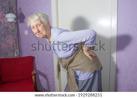 Elderly senior 75s woman with painful feelings massaging low back to reduce ache, backache discomfort. Diseases of older people, sciatic nerve injury concept Royalty-Free Stock Photo #1929288251