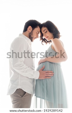Side view of man touching belly of pregnant wife in dress isolated on white