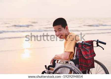 Asian special child on wheelchair on the sea beach with sunset on travel time in holiday family, Learning about nature around the sea, Lifestyle in education age kids, Happy disabled kid concept.