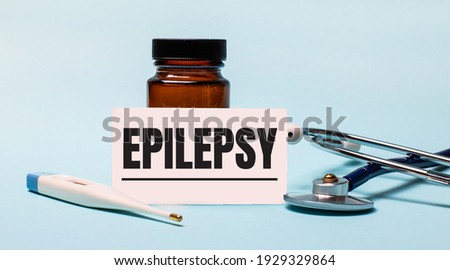 On a blue background - a bottle for pills, a stethoscope, an electronic thermometer and a card with the inscription EPILEPSY. Medical concept