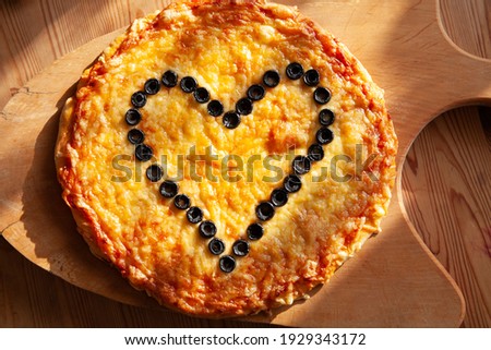 Golden coloured pizza with a shape of a heart made from black olives 