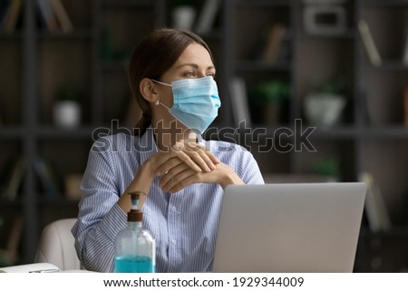 Female employee wear facial mask protect from coronavirus sit at desk work online on computer in office. Caucasian businesswoman in facemask from covid-19 pandemics at workplace. Corona concept. Royalty-Free Stock Photo #1929344009