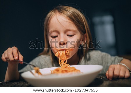 Hungry little girl appetite eating the bolognese pasta sucking it up to mouth in the low light kitchen table. 