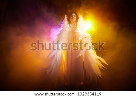 Brunette girl in an elegant dress and with white angel wings on a black background. Model, actress or dancer posing in the studio
