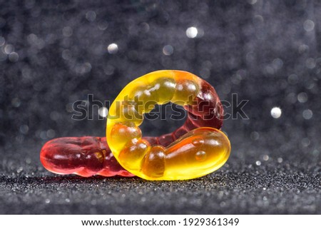 Close-up of a curled yellow-red gummy worm on a glittering blurred background.