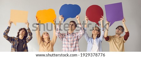 Group of young people standing on gray studio background, looking up at multicolored empty cardboard and paper mockup speech bubbles, giving feedback, sharing important message, expressing own opinion