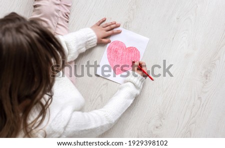 A little girl draws a heart on the floor. Top view. Copy space for text