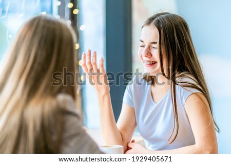 Girl in braces on teeth bursted into laugh sitting and talking with her friend in cafe.