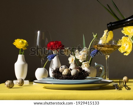 Easter table setting. There are plates and glasses on the table, and champagne is poured into one of the glasses. There are flowers in vases of different shapes. Table setting concept