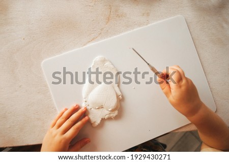 The hands of a small child who rolls out the clay to create a gift, a surprise for relatives and families. Child development, hobbies, clay hobby. Made by hands. Cozy home atmosphere.