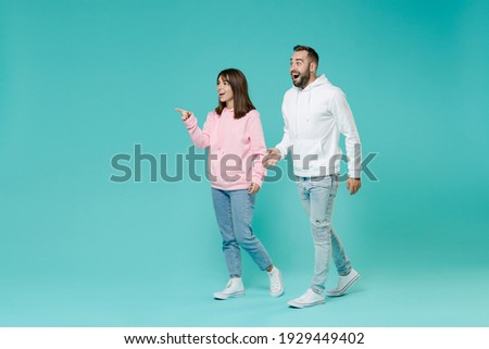 Full length side view of shocked excited young couple two friends man woman 20s wearing white pink casual hoodie pointing index finger aside isolated on blue turquoise wall background studio portrait