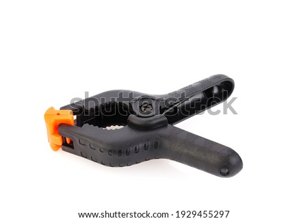 Plastic spring clamp isolated on white background. Clamping equipment. Working hand tool. Black and orange spring clamp. Closeup.