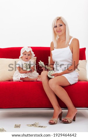 Mother and young daughter with a large wad of money dollars sit on a red sofa on a white background, copy space. High quality photo