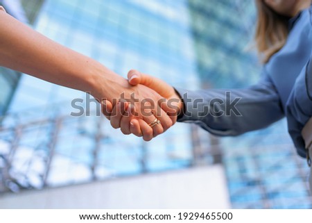 Woman handshaking outdoors over modern glass business building background, close-up picture