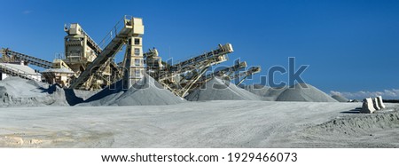Quarry machines and piles of gravel over blue sky. Stone crushing and screening plant, panoramic view Royalty-Free Stock Photo #1929466073