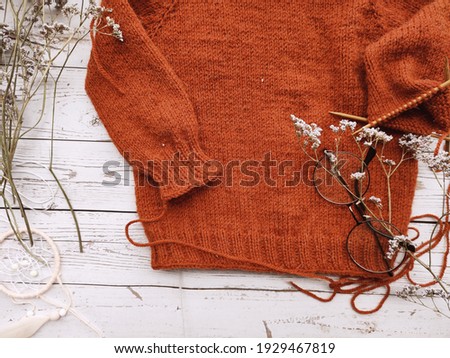 Mess on the knitter's table, unfinished projects and baby sweater on white wooden background