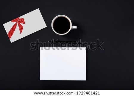 white envelope with a painted red bow is on the table next to a cup of coffee. white sheet of paper beside for writing.High quality photo