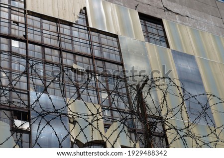 Barbed wire against the background of an abandoned industrial building, Soviet building, bottom view. Closed and guarded territory. Abandoned danger area.