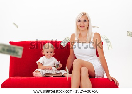 A happy mother and daughter in white clothes sit on a red sofa in the rain of dollars on a white background, a copy space. High quality photo