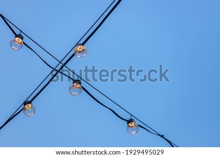 Selective focus of light bulb hanging on power cable line with blue clear sky as background, Erectic wire with lamp in evening with warm light.