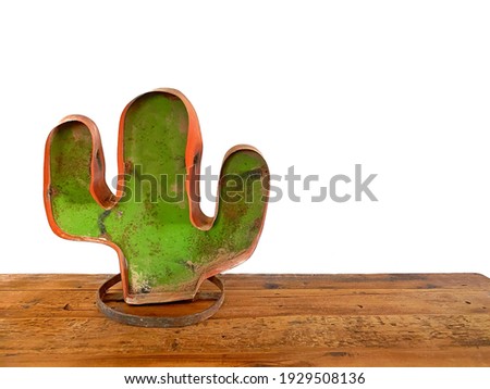 Background photo- Southwestern metal saguaro cactus statue with some rustic dirt at its base on a wooden table and white background with copy space.