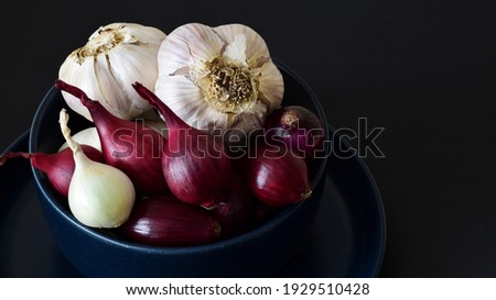 Garlic bulbs, red and white Pearl onions photographed in a navy blue colored bowl.  Selectively focused and photographed closely, this image is naturally lit.