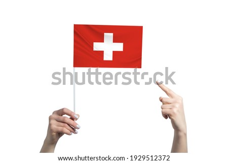 A beautiful female hand holds a Switzerland flag to which she shows the finger of her other hand, isolated on white background.