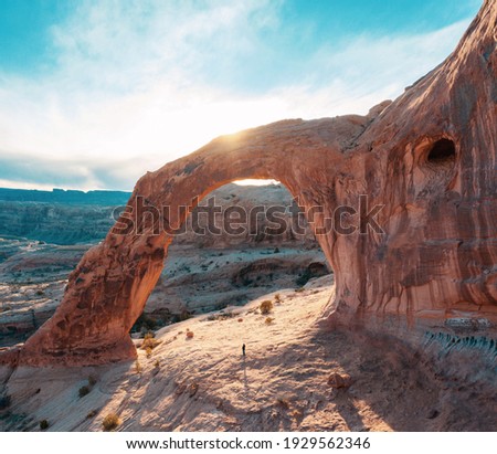 Beautiful sunset at Red Rock Arch in Moab. Aerial drone photo of Corona Arch in Utah with person standing underneath center. Royalty-Free Stock Photo #1929562346