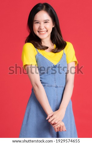 Asian girl Wear yellow shirt and short skirt pose in advertising and presenting goods and contents gesture with friendly smile face on red background