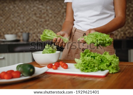Cropped image unrecognisable woman cooking healthy food at home kitchen - lettuce salad, cherry toatoes and cucumber