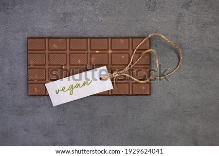 sweet bar of chocolate lies on a gray stone background with a label that says vegan and a vintage string
