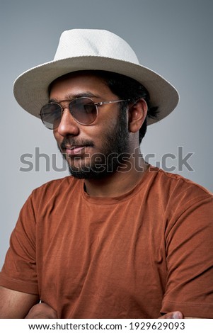 Closeup headshot of a fashionable hindu macho with hat and sunglasses posing in gray background.