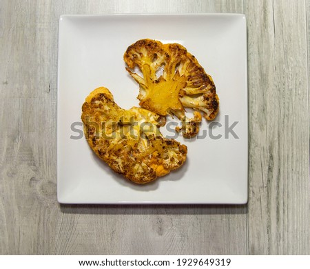 Two crispy roasted cauliflower steaks served on a white plate.